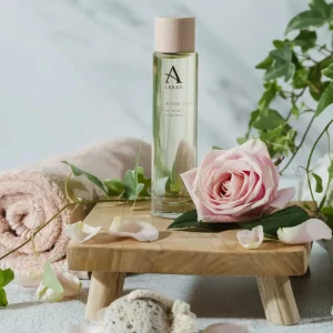 Arran After The Rain Bath & Body Oil bottle beside soft pink rose