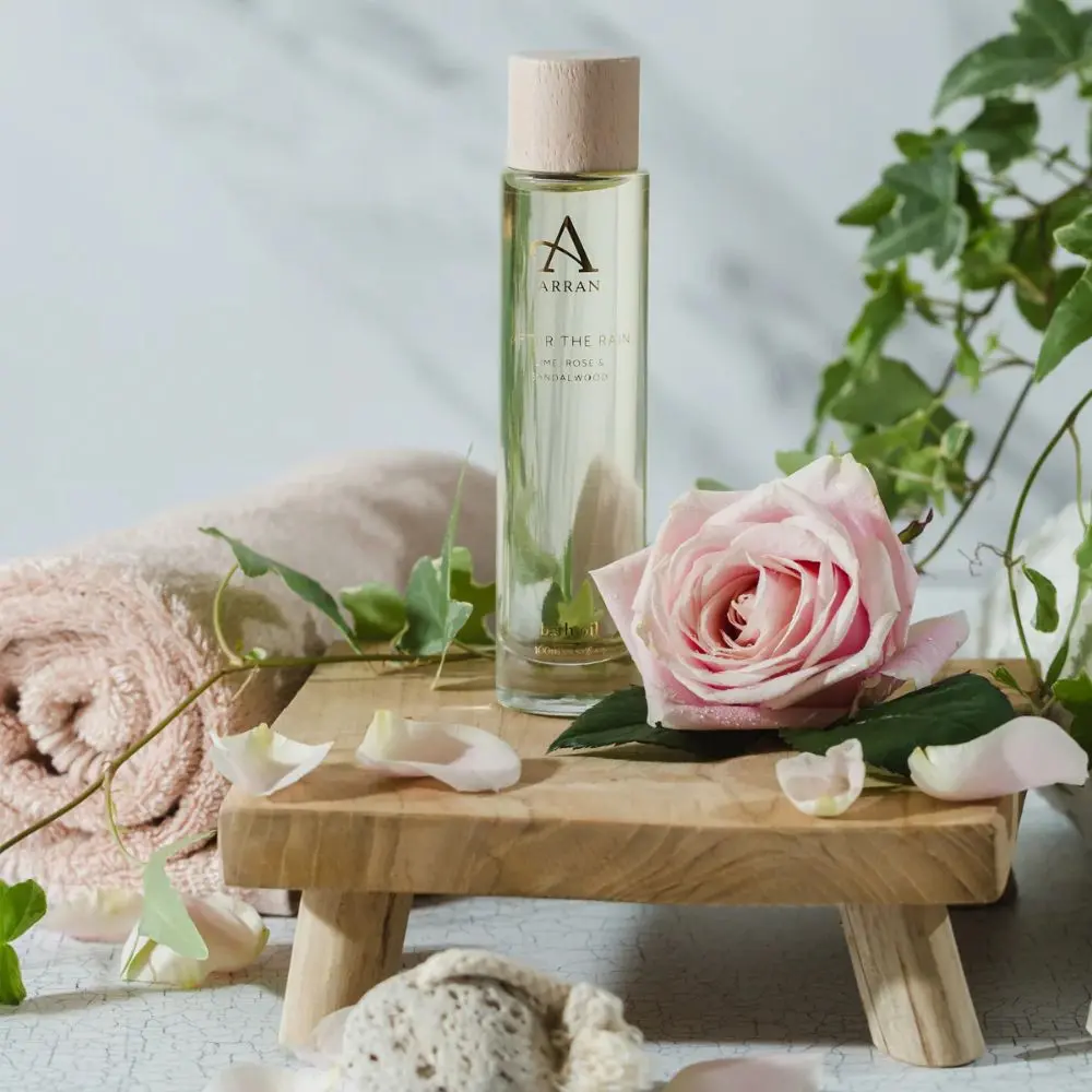 Arran After The Rain Bath & Body Oil bottle beside soft pink rose