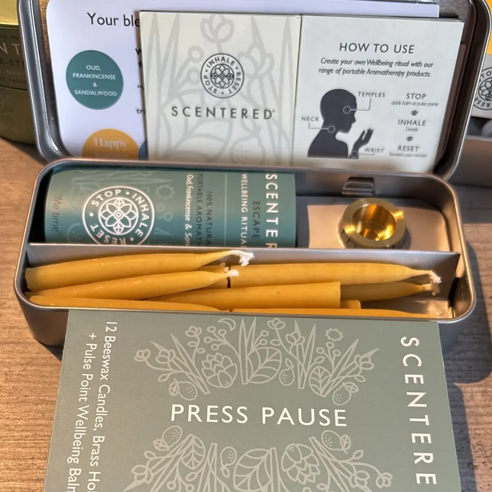 Scentered Press Pause Relaxation Set in an open tin with Escape balm, beeswax candles, brass holder and presentation sleeve.