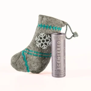 Scentered Sleep Well aromatherapy balm beside a grey felt Christmas stocking with turquoise embroidery and white snowflake.